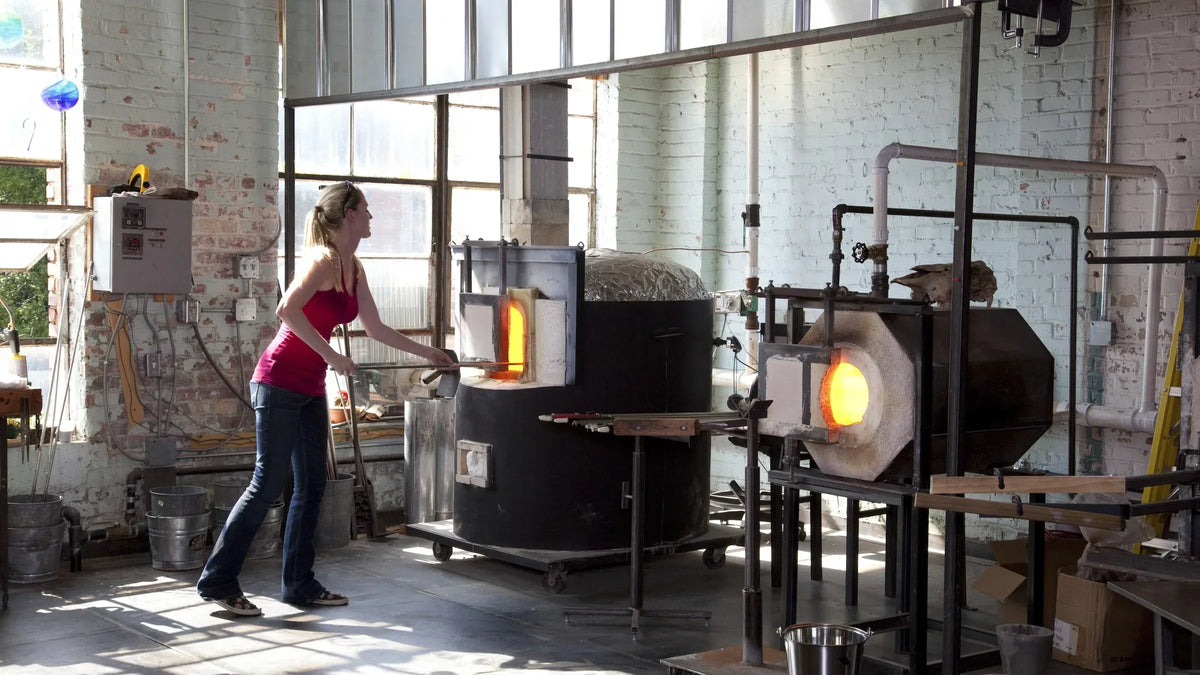 Glassblowers Susan Knecht and Allison Smith working beside a glowing furnace at Lowe Mill in Huntsville.